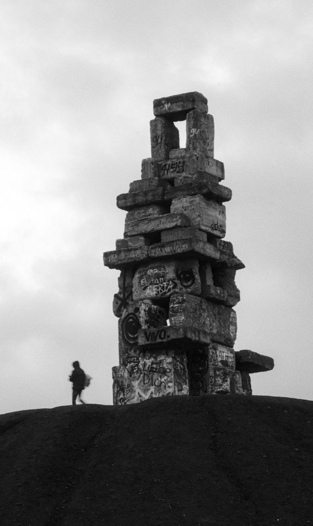 ภาพขาวดำของกองเศษหินเหมืองถ่านหินในเมืองเกลเซนเคียร์เชิน มีเสาหินสูงตั้งอยู่บนยอดเนินและคนเดินอยู่ด้านล่าง