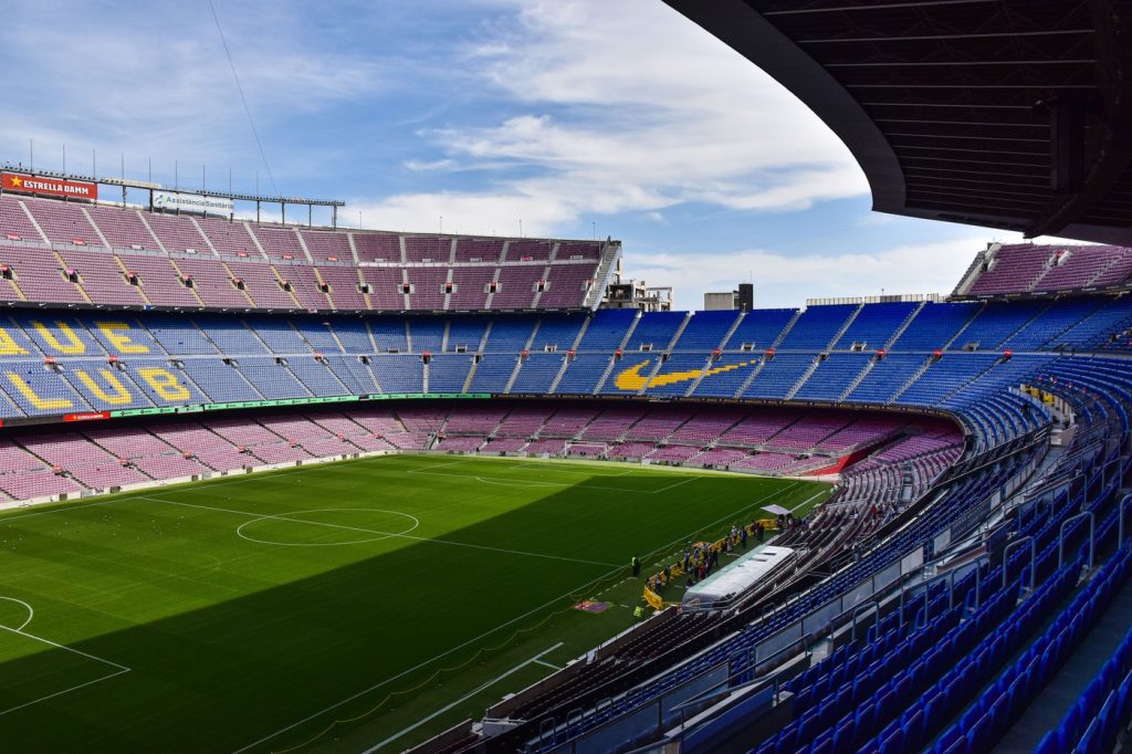 ภายในสนามคัมป์นูมองจากอัฒจันทร์สูง เห็นที่นั่งสีน้ำเงินและแดงเรียงเป็นแถวโค้งรอบสนามหญ้า