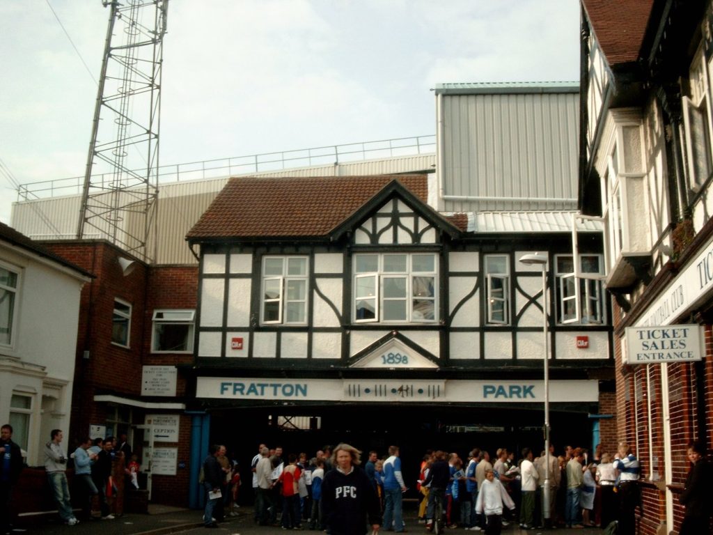 ทางเข้าสนามแฟรตตัน พาร์ค มีป้าย FRATTON PARK และแฟนบอลยืนรอเข้าชมเกม