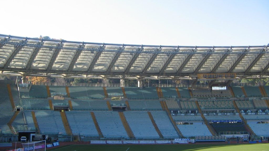 อัฒจันทร์และหลังคาของสนามโอลิมปิโกในกรุงโรม มองเห็นที่นั่งเรียงเป็นแถวและสนามหญ้าด้านล่าง